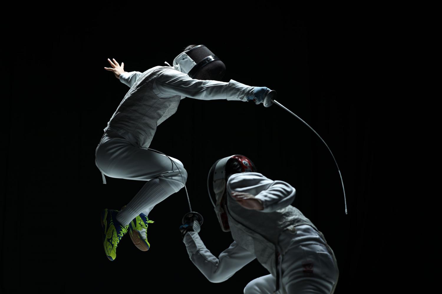 Two competitive fencers mid-combat against a black background, photographed with the Canon RF 70-200mm f2.8L IS USM lens Two competitive fencers mid-combat against a black background, photographed with the Canon RF 70-200mm f2.8L IS USM lens