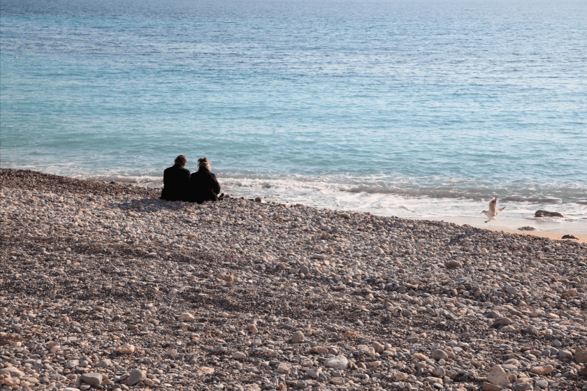 Couple sitting on a pebble beach, looking out to sea - photographed with the Canon EF 24-70mm f2.8L II USM lens