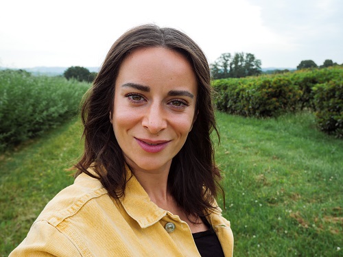 Selfie of young woman with dark hair standing in a Greenfield, shot with the Panasonic G100 Mirrorless Camera